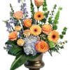 Mixed bouquet of orange roses, gerbera daisies, and blue flowers in a gold vase