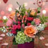 Pink and peach floral arrangement in a purple vase with heart decorations