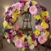 Colorful floral wreath on a black stand with pink, yellow, and purple blooms