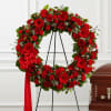 A dense circle of deep red roses, gerbera daisies and carnations forms