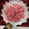 Handheld bouquet of pink roses wrapped in white paper with ribbons and pearl trim