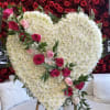 Heart-shaped white floral arrangement with pink roses on an easel