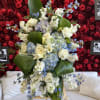 Large floral spray with white roses, blue blooms, and broad green leaves