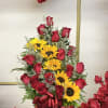 Basket arrangement of red roses and yellow sunflowers with a red ribbon