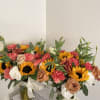 Two mixed flower arrangements in glass vases with sunflowers, roses, and carnations
