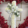 White floral cross arrangement on an easel with red rose backdrop