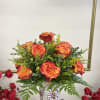 Orange-red roses in a patterned vase with a white ribbon