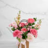 Pink roses and ranunculus arranged in a gift bag with a ribbon.