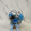 Blue roses in a small gift basket with a snowman ornament and pinecone