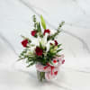 Red roses and white lilies in a glass vase with a pink teddy bear