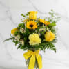 Yellow roses and mixed flowers in a glass vase with a yellow ribbon