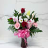 Bouquet of red roses, pink lilies, and white daisies in a vase with a pink bow