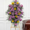 Tall standing spray of lavender roses and yellow daisies on an easel beside a wooden casket.