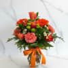 Orange and coral bouquet in a glass vase with a ribbon