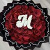 Round bouquet of red roses with a white floral monogram on black wrap