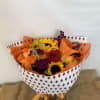 Bouquet of sunflowers, roses, lilies, and purple flowers wrapped in patterned paper