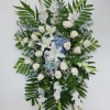 Standing floral spray with white lilies, roses, and blue accents