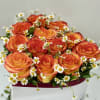 Low arrangement of orange and yellow roses with white daisies in a white hat box container