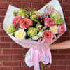 Bouquet of pink and cream flowers wrapped in pale paper with a ribbon