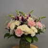 This arrangement includes cream roses, pink carnations, purple snapdragons, and delicate white