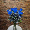 Blue roses arranged in a clear glass vase with mixed foliage