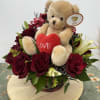 Teddy bear with a red heart surrounded by red roses in a basket