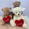 Three teddy bears holding red hearts on a round wooden base
