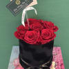 Red roses arranged in a black round box with a ribbon and card