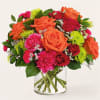 Mixed bouquet of orange, pink, and red flowers in a clear glass vase