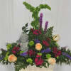 Mixed floral arrangement with peach roses, purple blooms, and a small angel statue
