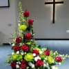 Tall floral arrangement with red roses and green accents in a church setting