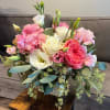Pink and white bouquet in a square vase with trailing greenery