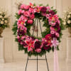 Pink and magenta floral wreath on a black stand with a pink ribbon bow