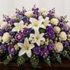 A graceful casket spray featuring white lilies, cream roses, rich purple blooms