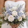 Soft white roses, pale blue blooms, and fresh greenery come together in