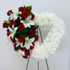 Heart-shaped floral wreath with red roses, white lilies, and white flowers on a stand