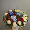 Mixed bouquet of red roses, blue hydrangeas, white carnations, and pale lilies in a white vase