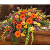 Colorful floral casket spray with orange gerberas, yellow callas, and purple accents