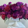 Purple and pink floral arrangement in a white pedestal vase