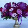 Purple and pink flower arrangement in a gold pedestal vase