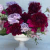 Deep burgundy and lavender flowers arranged in a white pedestal vase