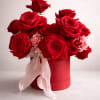 Red roses arranged in a round red box with a pale ribbon