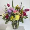 Colorful mixed bouquet with pink roses, yellow carnation, tulips and lavender blooms in a clear glass vase