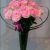 Pink roses arranged in a tall glass vase with decorative loops