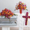 Bright gerbera daisy funeral arrangements on a casket and easel cross.