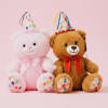Two plush teddy bears wearing party hats and bows on a pink background