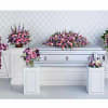 Floral funeral display with a cross, casket spray, and standing sprays in pink and purple