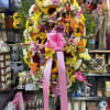 Large standing floral spray with lilies, sunflowers, roses, and a pink ribbon