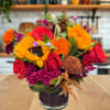 Mixed bouquet of sunflowers, red roses, and orange blooms in a glass vase