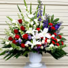 Large arrangement of red roses, white lilies, and purple flowers in a white urn